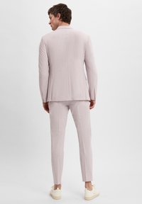 Helles rosa Sakko und Hose aus strukturiertem Stoff, mit taillierter Passform. Getragen mit cremefarbenen Schuhen. Rückansicht.