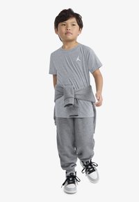 Gray cotton T-shirt with a small white logo, paired with gray sweatpants and black-and-white high-top sneakers, with a sweater tied around the waist.
