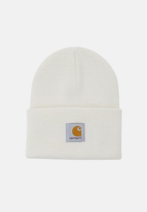 Gorro de punto en color crema, con un dobladillo doblado y un parche de logo cuadrado con acentos amarillos y grises. Textura suave, diseño sencillo.