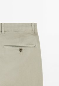 Ljust grå byxor med en strukturerad tyg, som har en bakficka med en knappstängning och bältesöglor på midjan.