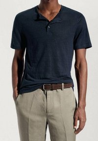 Granatowa koszulka polo z krótkim rękawem i zapinanym kołnierzykiem, w połączeniu z jasnobeżowymi spodniami. Brązowy skórzany pasek dodaje kontrastowy akcent.