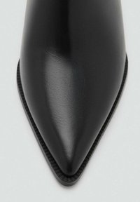 Črni čevlji z ostrim prstom iz gladkega usnja s teksturirano površino. Imajo tanko, povišano podplato in vitko obliko.