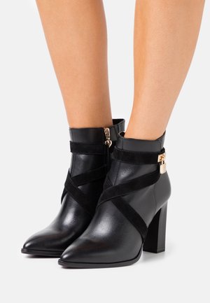 Schwarze Knöchelstiefel aus Leder und Wildleder mit spitzem Zehenbereich, Blockabsatz und Querriemen mit einem goldenen Verschluss, für einen sicheren Sitz entworfen.