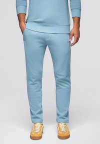 Lichtblauwe joggers van een zachte katoenmix; slim fit met zakken; gecombineerd met beige en gele sneakers met witte veters.