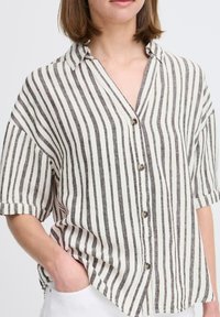 Camicia a righe a maniche corte in crema e grigio scuro. Presenta un colletto, chiusura a bottone e una vestibilità rilassata con tasca.