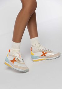 White and pastel sneakers with orange accents, suede and mesh materials, triangular blue and yellow details, and textured soles.
