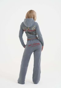 Grå denimkort hoodie med snörning och broderad text på baksidan, i kombination med löst sittande matchande sweatpants med elastisk midja och logodetalj.