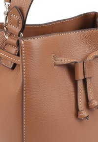 Sac seau en cuir marron avec une finition texturée, doté d'une fermeture à cordon, de coutures contrastantes et d'une bandoulière amovible.