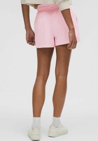 Pink shorts made of lightweight fabric, featuring a relaxed fit, elastic waistband, and side pockets. Worn with white sneakers and socks.