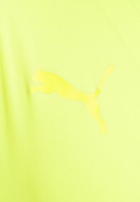 Tessuto atletico giallo neon con un logo Puma lucido e in rilievo di una tonalità più chiara, caratterizzato da un aspetto liscio e testurizzato.