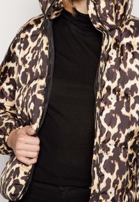 Chaqueta de plumón con un patrón de leopardo en tonos de marrón y beige, con cierre delantero y capucha. Material ligero y texturizado.