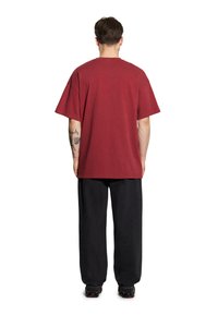 Burgundowa, oversize koszulka bawełniana z okrągłym dekoltem i krótkimi rękawami, zestawiona z czarnymi luźnymi spodniami.