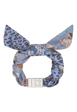 Chouchou en tissu bleu avec motifs floraux et imprimé léopard, avec un nœud et une fermeture rectangulaire dorée et blanche ornée d'un dessin de trèfle.