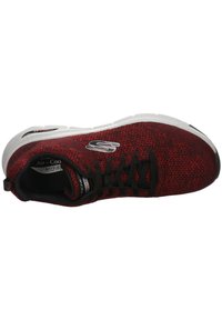 Scarpa sportiva rossa in maglia con accenti neri, dotata di una tomaia texturizzata, chiusura con lacci e una suola bianca imbottita con elementi di design.