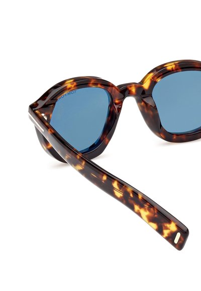 Kočičí sluneční brýle z želvoviny s modrými čočkami, s elegantním tvarem a lesklým povrchem. Rám je silný s texturovanými detaily.