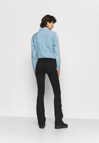 Camisa de ganga azul clara com colarinho, mangas longas e punhos com botão, combinada com jeans pretos à boca de sino e botas pretas robustas.