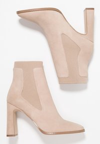 Botines de ante beige con punta puntiaguda y tacón grueso alto, con paneles laterales elásticos y textura suave.