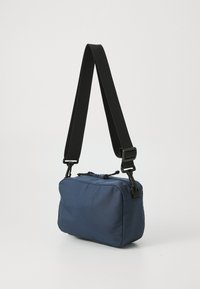 Dunkelblaues Stoff-Crossbody-Bag mit rechteckiger Form, schwarzem verstellbarem Schultergurt, Reißverschluss oben und minimalistischem Design.