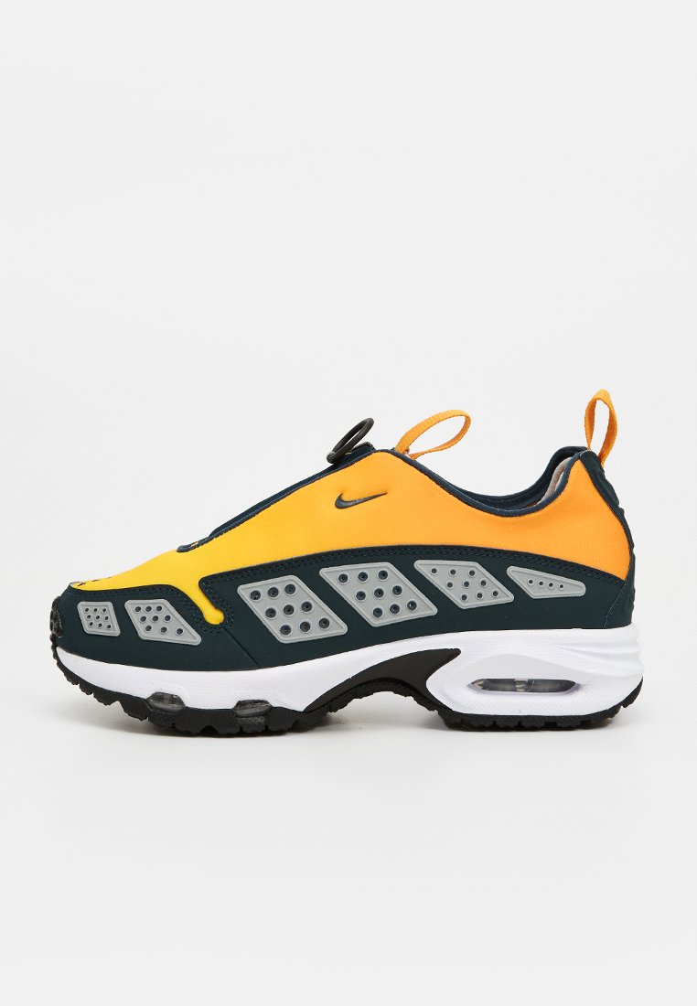 Zapatilla deportiva con una parte superior amarilla y verde oscuro, con detalles en gris y perforaciones. Media suela blanca con amortiguación de aire visible.