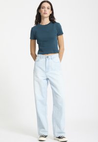 Beskaaret teal t-shirt med diskret tekst og lyseblå vidde jeans. Klassisk pasform, blødt stof og kontrasterende sorte og hvide sneakers.