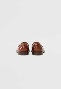 Chaussures en cuir marron avec une finition lisse, dotées d'arrières arrondis, de coutures minimales et d'une semelle foncée contrastante.