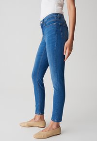 Jean skinny bleu en denim, avec une texture lisse, une taille standard et un design à cinq poches. Assortis à des chaussures plates nude.