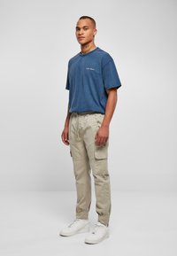 Blå bomull t-skjorte med rund hals, kombinert med beige cargo bukser med sidelommer. Skoene er hvite sneakers med et teksturert design.
