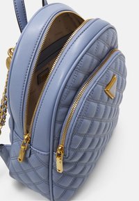 Kleine lichtblauwe leren rugzak met doorgestikte structuur, gouden ritsen en logoplaatje, gedeeltelijk open hoofdvak met een beige voering met merklogo.