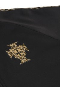 Μαύρο ύφασμα που διαθέτει έναν υφαντό χρυσό έμβλημα με σχέδιο ασπίδας και σταυρού, απεικονίζοντας τα γράμματα "F.P.F." και ένα μοτίβο από ασπίδες.