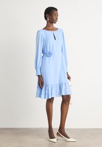 Lichtblauwe jurk met lange, geaccentueerde mouwen, keyhole-halslijn, stippenpatroon, bloemaccent op de taille en gerimpelde zoom.