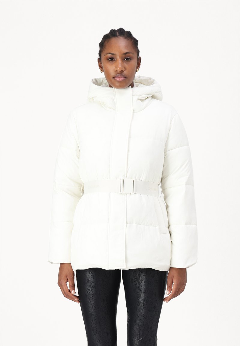 Hvid pufferjakke med høj krave, bælte i taljen og to frontlommer. Glat tekstur med en blank finish. Inkluderer en hætte.