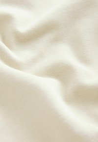 Tessuto color crema con una texture liscia e una lieve elasticità, caratterizzato da sottili motivi a maglia e una morbida caduta.