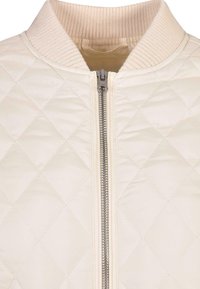 Chaqueta bomber acolchada en crema claro, con cuello de canalé y cremallera central. La superficie presenta un patrón de diamantes y una textura suave.
