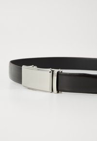 Ceinture en cuir noir avec une boucle en métal argenté rectangulaire au surface lisse et au design minimaliste.