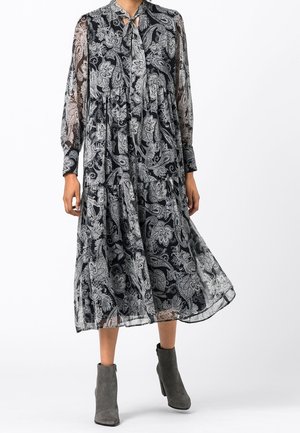 Vestido midi con patrón de cachemira en blanco y negro, con mangas largas transparentes y lazo en el cuello, combinado con botines de gamuza gris.