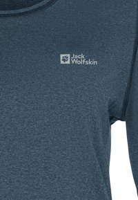 Nahaufnahme eines blauen strukturierten Sweatshirts mit dem weißen Jack Wolfskin-Logo und dem Pfotenabdruck auf der oberen Brust.