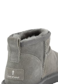 Grijze suède enkelboot met een zachte faux bont voering, gestikte details, een stoffen trekband en een rubberen zool. Logo label aan de zijkant.