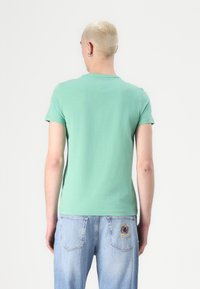 Mint green short-sleeve t-shirt with a straight cut and round neckline, paired with light blue denim jeans featuring embroidered accents.