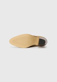 Scarpa in suede beige con punta arrotondata e suola in gomma liscia. La suola ha un leggero tacco e una superficie texturizzata per una maggiore aderenza.