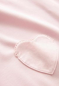 Tissu rose doux avec un patch en forme de cœur cousu, présentant des bords festonnés délicats en fil rose assorti.