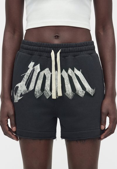 Μαύσες σορτς με ελαστική μέση, φθαρτό λευκό τυπωμένο κείμενο και κρεμ κορδόνια, φορεμένα με λευκό κοντό μπλουζάκι.