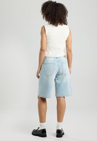 Light blue denim shorts with a relaxed fit, featuring rear pockets and a textured white sleeveless top, paired with black glossy shoes.