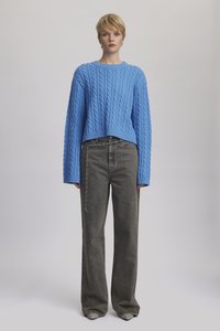Világoskék, cable-knit pulóver hosszú ujjakkal, magas derékú, sötétszürke, bő szárú farmernadrággal párosítva, lánc részletekkel.