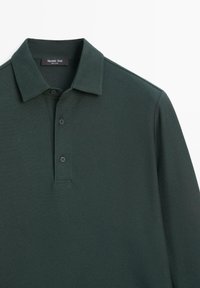 Dunkelgrünes Poloshirt aus einem strukturierten Stoff, mit einem Drei-Knopf-Verschluss und einem klassischen Kragen. Das Etikett trägt die Aufschrift "Massimo Dutti."