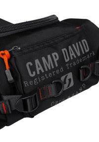 Black fabric shoulder bag with orange zipper pull, featuring logo and text, adjustable straps, and red stitching details.