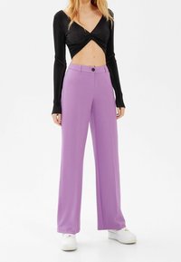 Černé dlouhé rukávy zkrácené tričko s krouceným předním dílem; vysoké široké kalhoty v levandulové barvě; spárované s bílými teniskami.