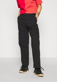 Zwarte cargo broek met een elastische tailleband, zijzakken en een relaxte pasvorm, gecombineerd met een gekleurde rode en roze cropped t-shirt.