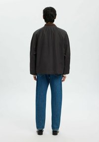 Svart lättviktig jacka med en brun krage, lös passform och rak ryggdesign, kombinerad med blå raka jeans och svarta skor.