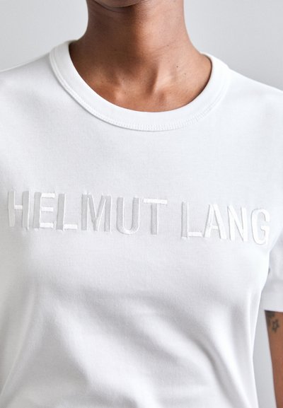 Valkoinen puuvillapaita, jonka rinnassa on brodeerattu "HELMUT LANG" samansävyisellä langalla. Yksinkertainen pyöreä pääntie ja sileä, pehmeä rakenne.