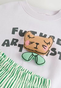 Jasnofioletowy sweatshirt z napisem "FUTURE ARTIST", z haftowaną łatą w kształcie brązowego misia oraz zielonymi akcentami w postaci liści. Na dole znajduje się paskowana zielona spódnica.